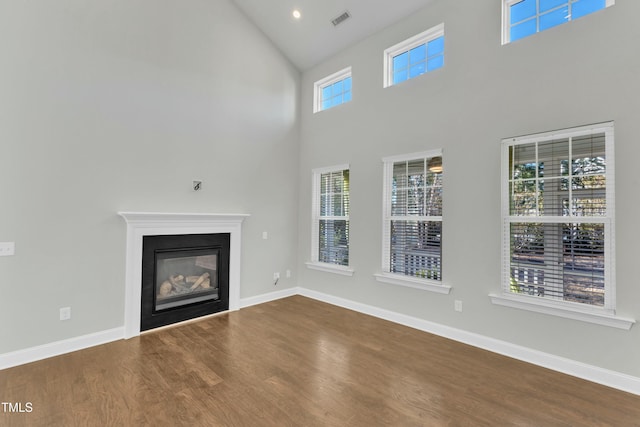 unfurnished living room with a glass covered fireplace, visible vents, baseboards, and wood finished floors