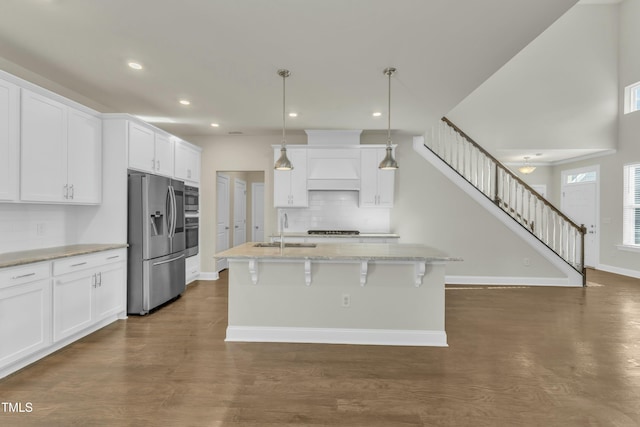 kitchen with white cabinetry, premium range hood, appliances with stainless steel finishes, and a sink