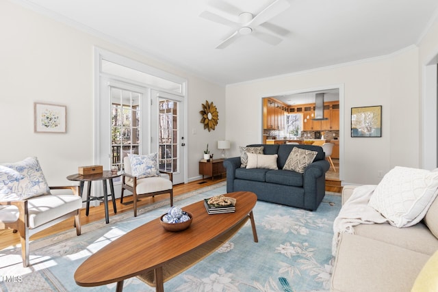 living area with ceiling fan, light wood-style flooring, baseboards, and ornamental molding