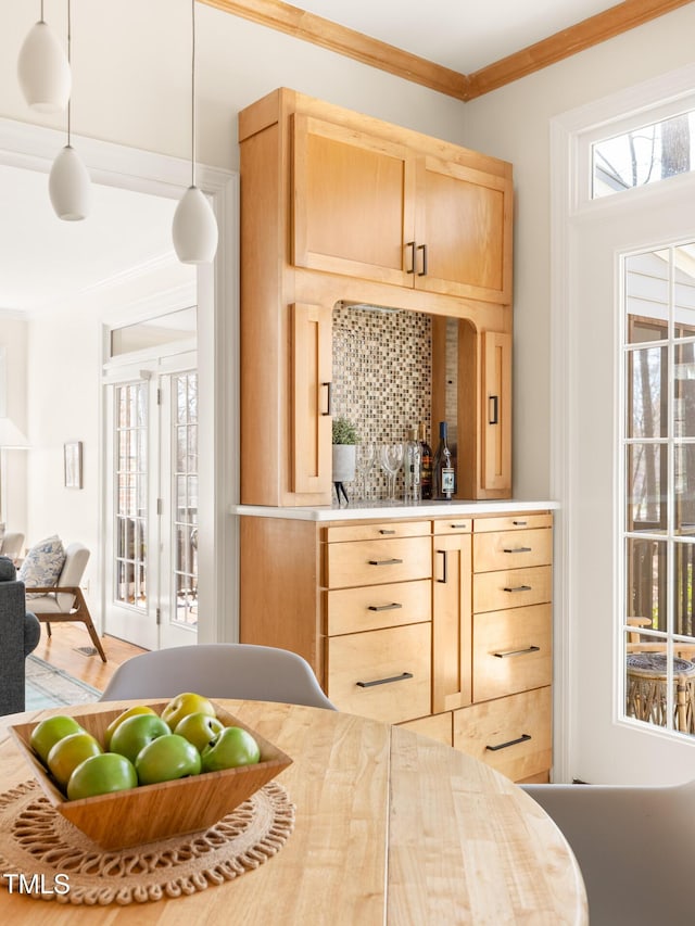 interior space with light brown cabinets, decorative backsplash, hanging light fixtures, light countertops, and crown molding