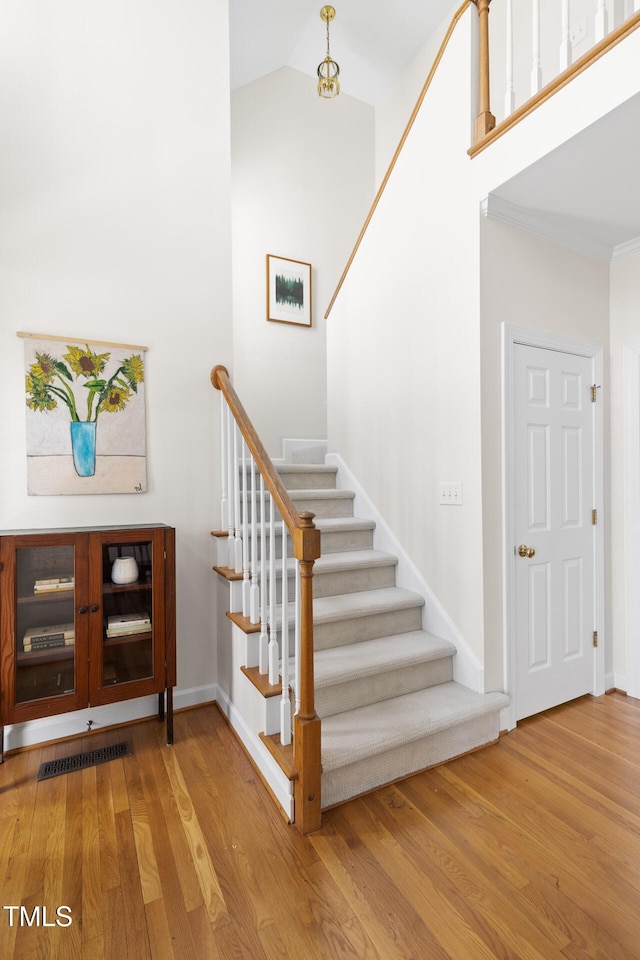 stairway with baseboards, high vaulted ceiling, and wood finished floors