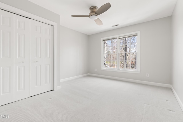 unfurnished bedroom featuring visible vents, baseboards, light colored carpet, a closet, and a ceiling fan