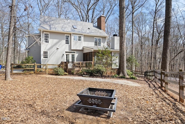 rear view of property featuring a fenced backyard, a fire pit, a sunroom, a wooden deck, and a chimney