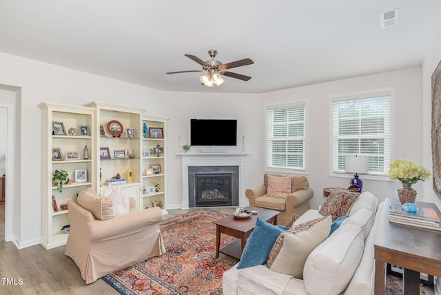 living area featuring wood finished floors, baseboards, visible vents, a fireplace with flush hearth, and ceiling fan