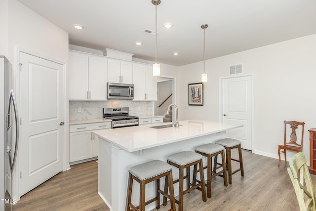 kitchen with visible vents, a sink, stainless steel appliances, a breakfast bar area, and decorative backsplash