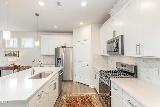 kitchen featuring light wood finished floors, an island with sink, white cabinets, stainless steel appliances, and a sink