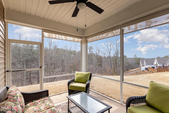 sunroom / solarium featuring wooden ceiling, a healthy amount of sunlight, a wooded view, and ceiling fan