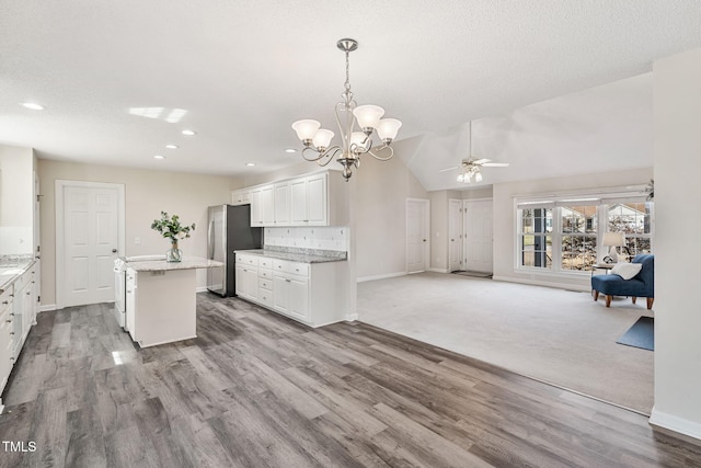 kitchen with ceiling fan with notable chandelier, a kitchen island, open floor plan, freestanding refrigerator, and white cabinets