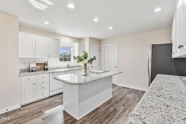 kitchen featuring wood finished floors, a kitchen island, white dishwasher, freestanding refrigerator, and white cabinets