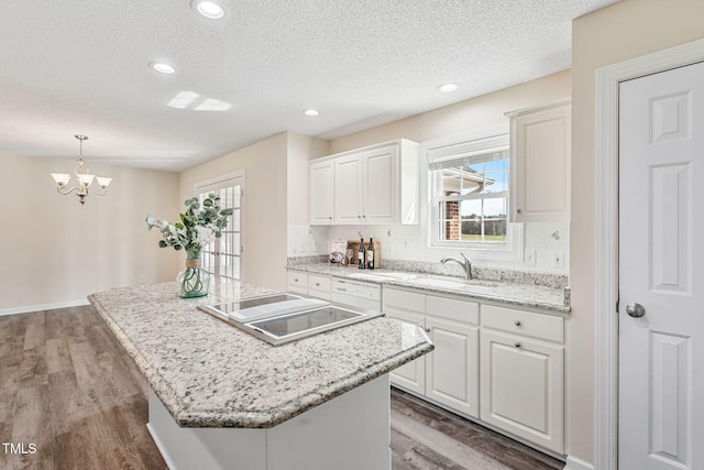 kitchen featuring wood finished floors, an inviting chandelier, a sink, white cabinets, and black electric stovetop