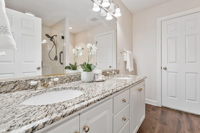 full bath with double vanity, wood finished floors, walk in shower, and a sink