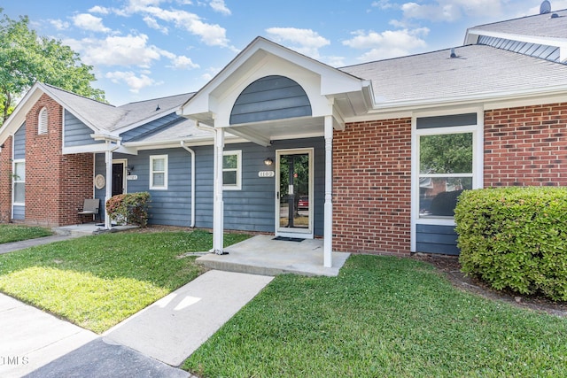 view of front of home featuring brick siding, a shingled roof, and a front yard