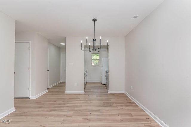 unfurnished dining area featuring light wood-style floors, baseboards, and a chandelier
