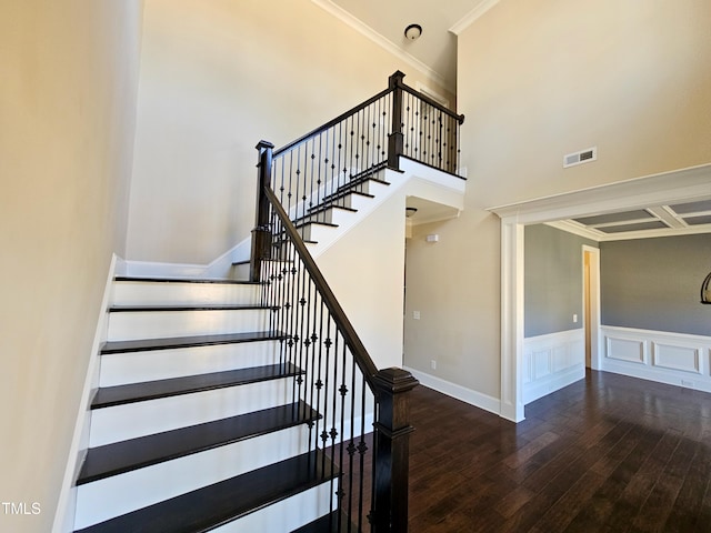 staircase with hardwood / wood-style floors, visible vents, a towering ceiling, wainscoting, and crown molding