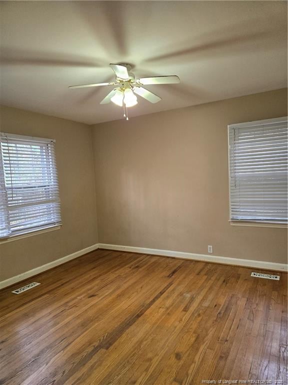 spare room featuring hardwood / wood-style flooring, baseboards, visible vents, and ceiling fan