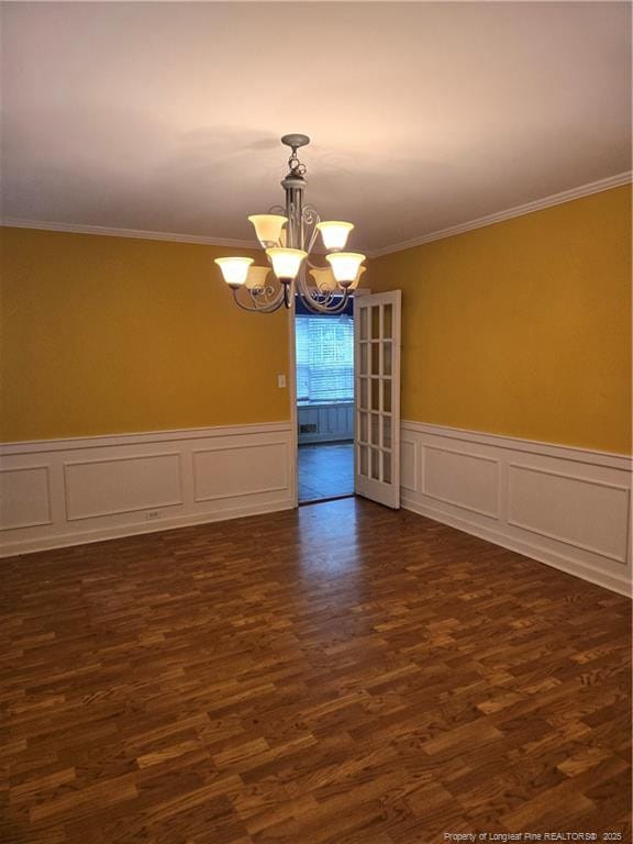 spare room with wainscoting, an inviting chandelier, ornamental molding, and dark wood-style flooring