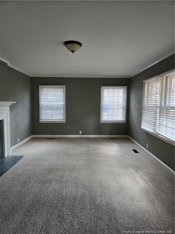 unfurnished living room featuring baseboards, a fireplace with flush hearth, carpet, and crown molding