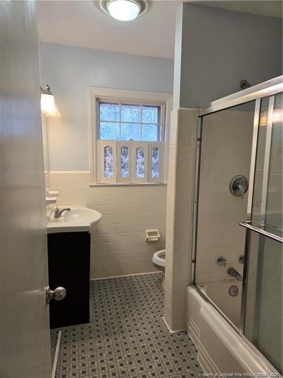 bathroom with a wainscoted wall, toilet, vanity, enclosed tub / shower combo, and tile walls