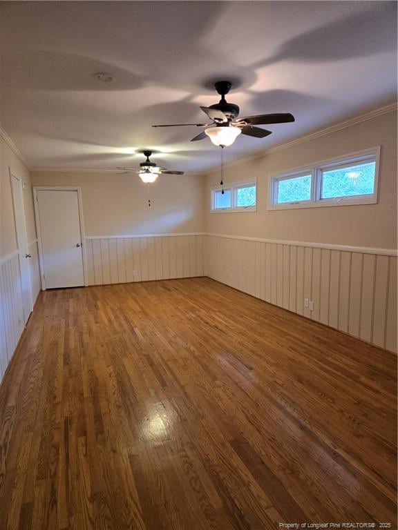 empty room with wood finished floors, wainscoting, and crown molding