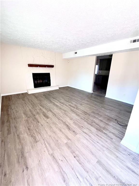 unfurnished living room with visible vents, a fireplace with raised hearth, a textured ceiling, wood finished floors, and baseboards