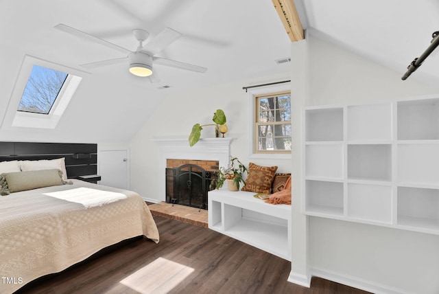 bedroom with visible vents, vaulted ceiling with skylight, a fireplace, wood finished floors, and a ceiling fan