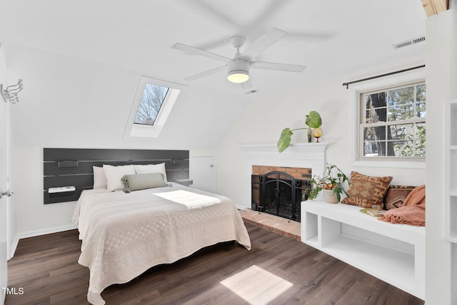 bedroom with visible vents, vaulted ceiling with skylight, a fireplace, wood finished floors, and a ceiling fan