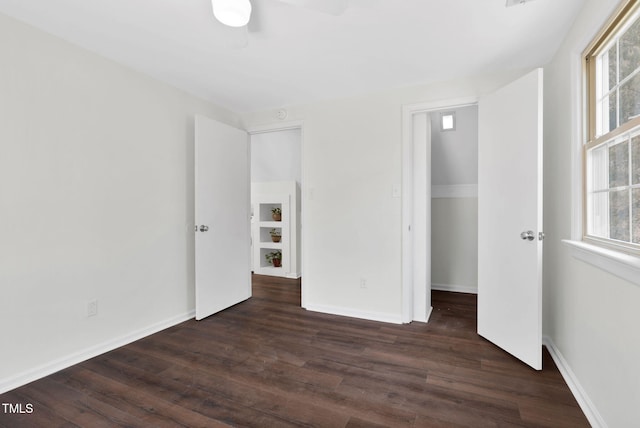 unfurnished bedroom with a walk in closet, multiple windows, baseboards, and dark wood-style flooring