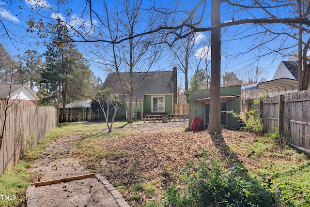 rear view of property with an outbuilding, a fenced backyard, a carport, and a chimney