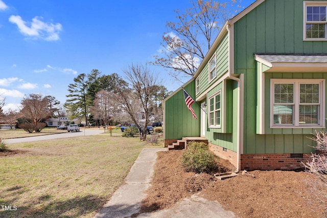 view of home's exterior with a shingled roof, a lawn, board and batten siding, and crawl space