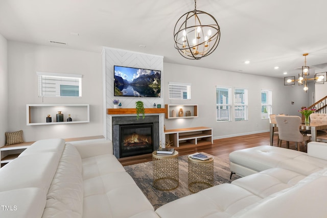 living room with a glass covered fireplace, visible vents, an inviting chandelier, and wood finished floors