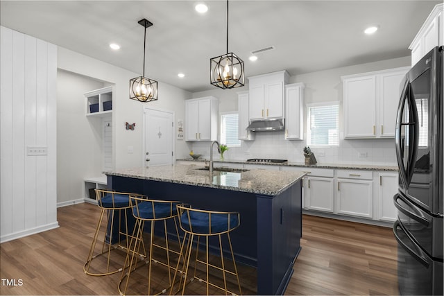 kitchen featuring visible vents, a breakfast bar, a sink, under cabinet range hood, and freestanding refrigerator