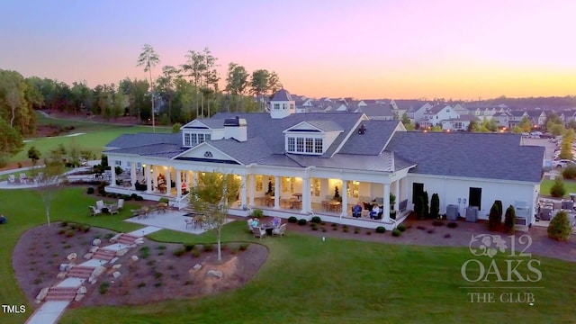 back of house at dusk featuring a residential view, a patio, a lawn, and central AC unit