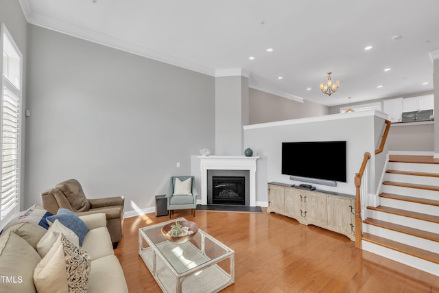 living area with stairway, light wood-style flooring, a glass covered fireplace, crown molding, and a notable chandelier