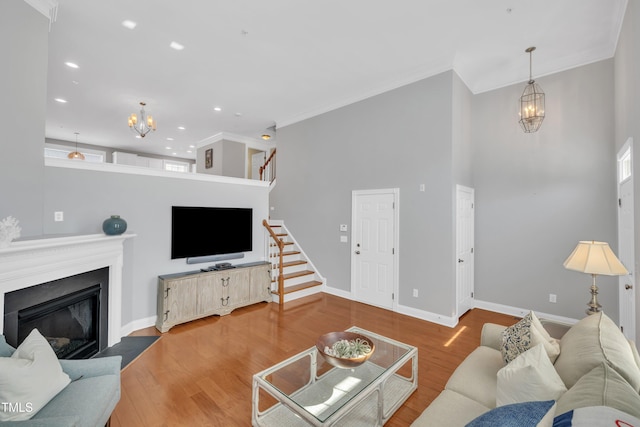 living area with a notable chandelier, wood finished floors, stairs, and a glass covered fireplace