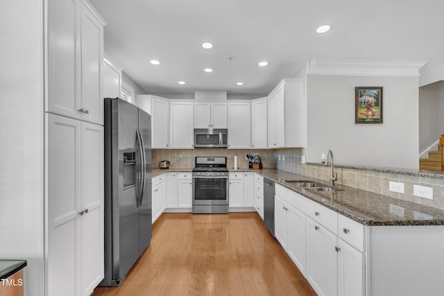 kitchen with a sink, dark stone countertops, stainless steel appliances, a peninsula, and white cabinets