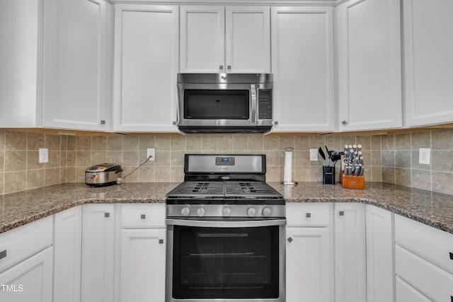 kitchen with stainless steel appliances, dark stone counters, tasteful backsplash, and white cabinetry