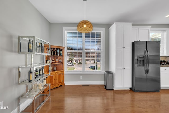 kitchen featuring wood finished floors, baseboards, visible vents, stainless steel fridge with ice dispenser, and white cabinets