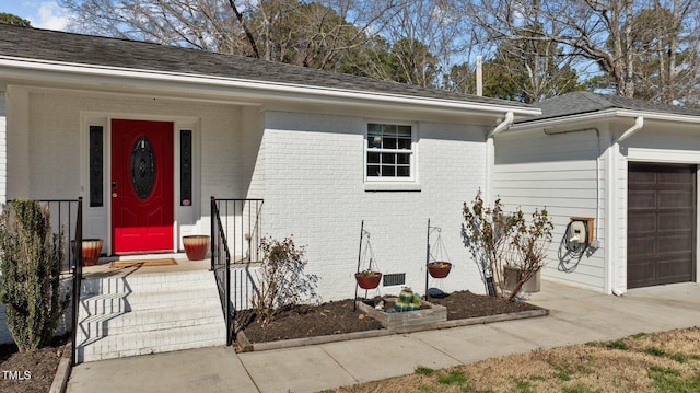 property entrance featuring brick siding, a garage, and roof with shingles