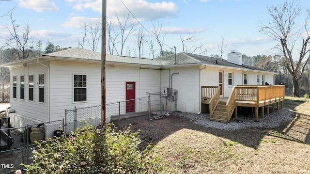 rear view of property featuring a deck, fence, a shingled roof, brick siding, and a chimney