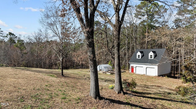 view of yard with a storage shed, a detached garage, an outbuilding, and a wooded view