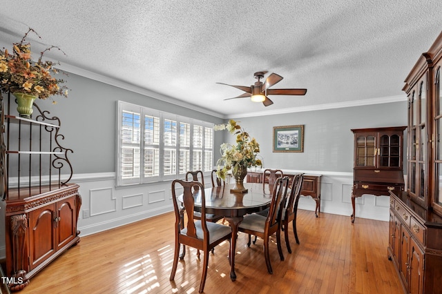 dining room featuring crown molding, a ceiling fan, a wainscoted wall, and light wood finished floors