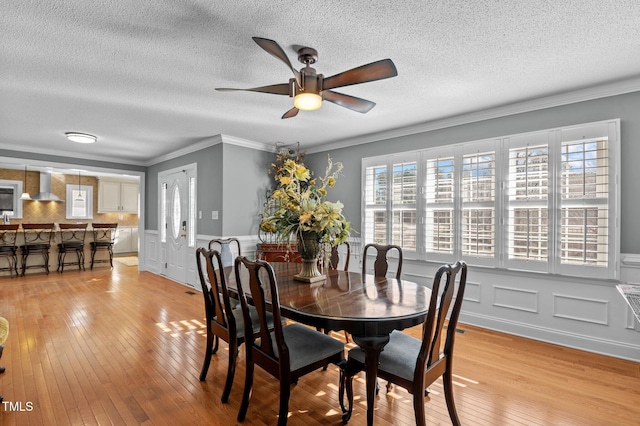 dining room with crown molding, light wood-style flooring, a wainscoted wall, and a textured ceiling