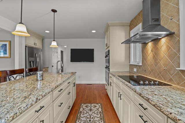 kitchen featuring light stone counters, a sink, black appliances, dark wood-type flooring, and wall chimney exhaust hood