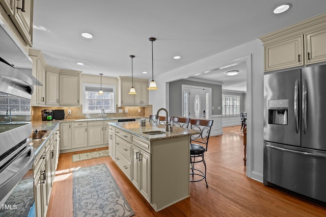 kitchen with a kitchen bar, cream cabinetry, a sink, stainless steel fridge, and light stone countertops