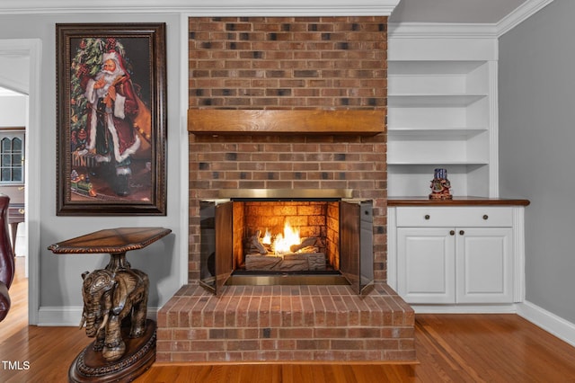 interior details featuring built in features, wood finished floors, baseboards, ornamental molding, and a brick fireplace