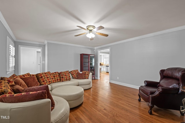 living room with a ceiling fan, wood finished floors, baseboards, and ornamental molding