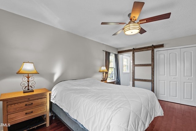 bedroom with a ceiling fan, wood finished floors, a closet, a textured ceiling, and a barn door