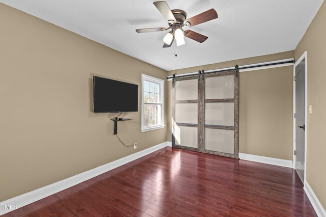 unfurnished bedroom with ceiling fan, a barn door, baseboards, and wood finished floors