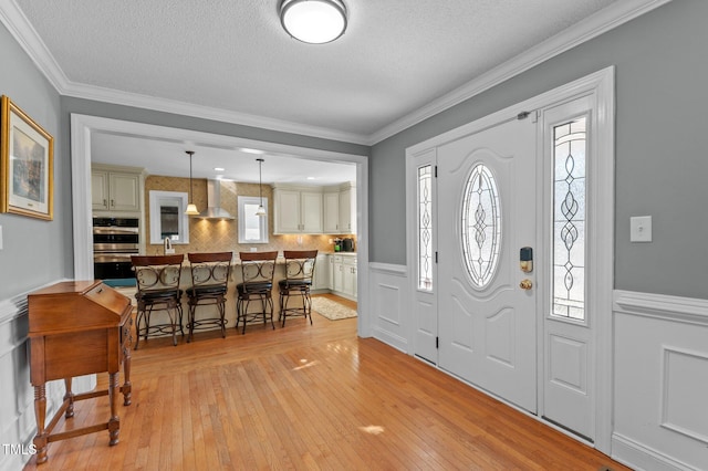 entryway with a textured ceiling, crown molding, light wood-type flooring, and wainscoting