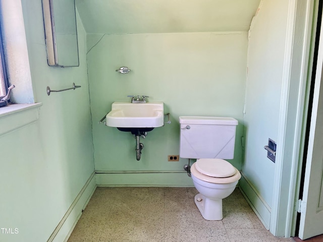 half bathroom with toilet, speckled floor, baseboards, and a sink